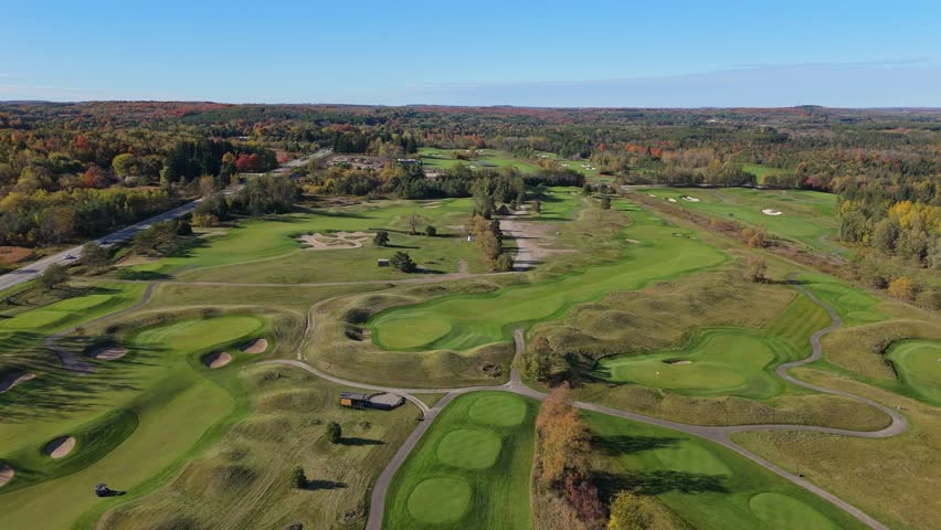 Aerial footage of a wide golf course surrounded by rolling fairways, sand bunkers, forest edges, and autumn colors in Caledon, Ontario.