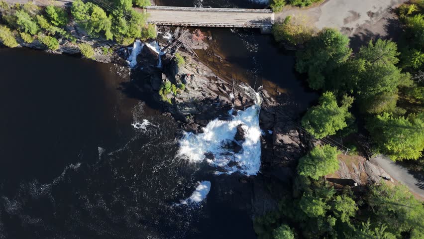 Aerial shot over High Falls on the Muskoka River, capturing cascading water, rocky terrain, surrounding forest, dam, and the bridge spanning the powerful flow in Muskoka, Ontario.
