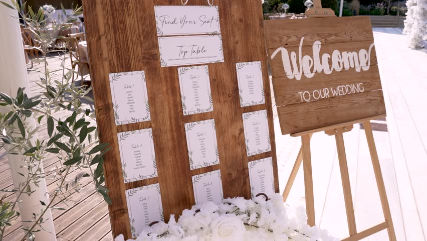 A beautiful outdoor wedding setup features a wooden seating chart for guests to find their seats. The welcome sign adds a charming touch to the festive atmosphere.
