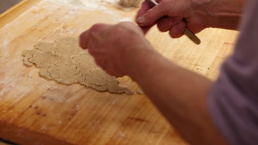  Elderly woman’s hands placing cut cookie dough shapes on tray showing real Christmas baking moment