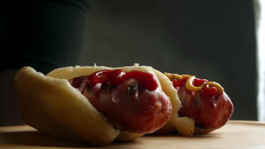 Cinematic food shot captures slow squeeze of mustard over juicy sausage, highlighting texture of bun, grill marks and glossy sauces for appetizing fast food promo.