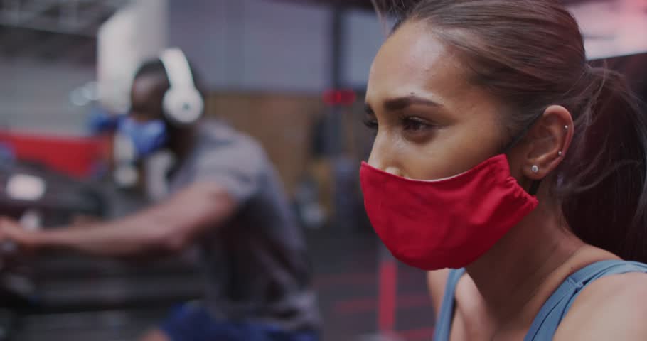 Woman wearing red mask in gym session starting red HUD icons sliding over mask signaling connection. Profile, fitness, overlay, headphones, gaze, cinematic, promo