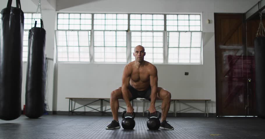 Man shifting weight, cleaning kettlebell to rack then lowering for fitness, golden streaks over man. Bells, lift, training, gym, studio, strength, focus