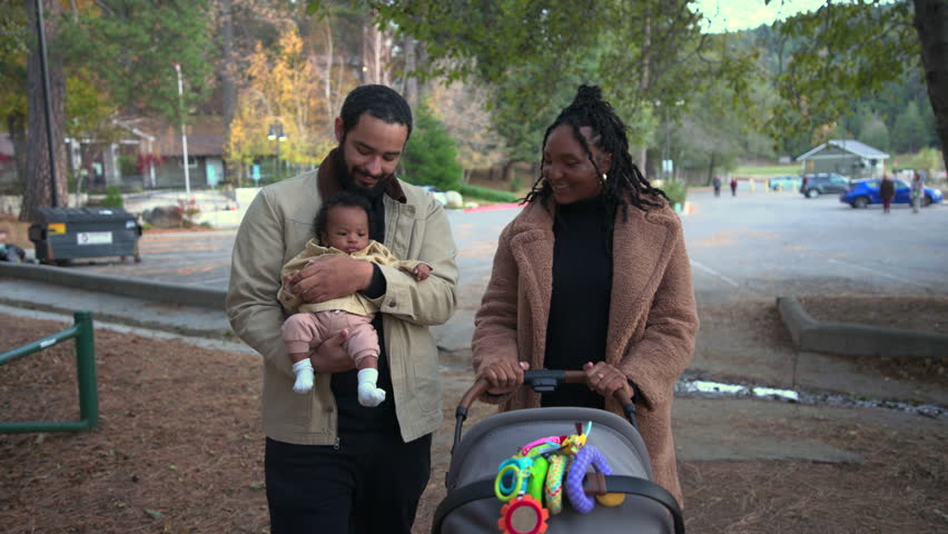 Bright outdoor scenery shows cheerful parents enjoying a slow stroll with a stroller while the father holds their newborn baby, surrounded by soft fall tones and a relaxed neighborhood vibe.