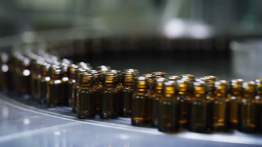 Close-up of medicines being produced in glass bottles on automated pharmaceutical production lines, showcasing modern drug manufacturing.