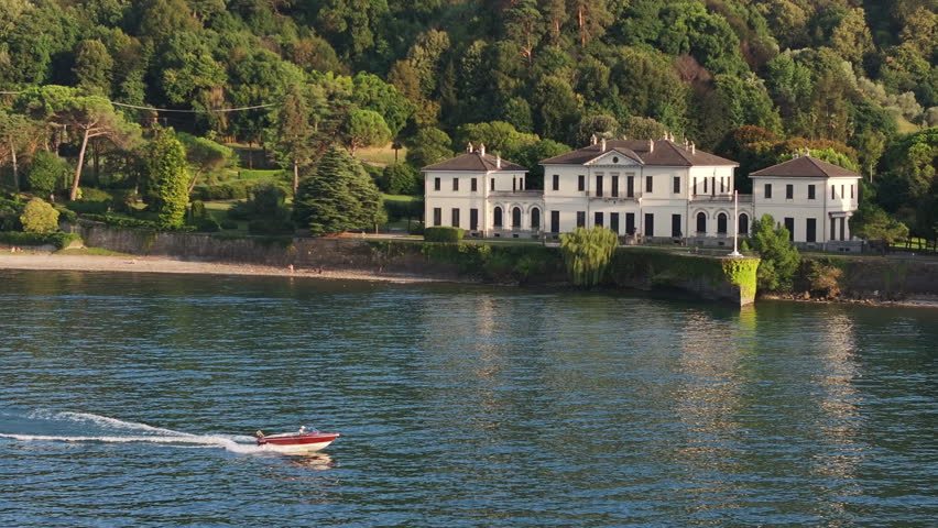 luxury villa by crystal blue lake, white neoclassical house nestled in dense green trees, calm water reflecting sunlight, red boat