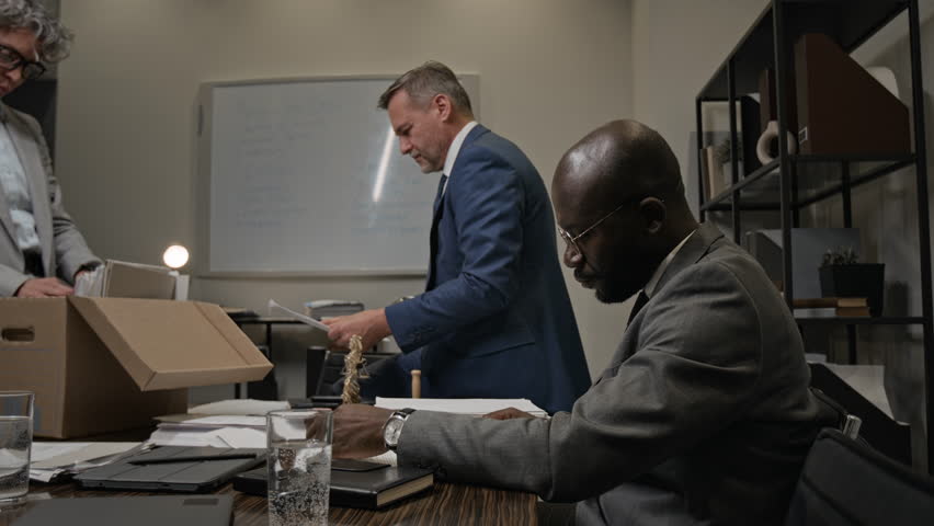 Medium shot of multiethnic attorneys working together at night in office, searching for precedents in archives, senior male partner finding information in case file and giving high fives to colleagues