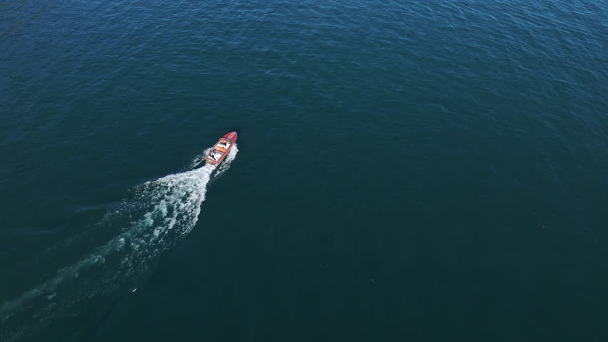 aerial view red speedboat crossing deep blue sea, steady diagonal wake trail, long transit line across calm water, commercial