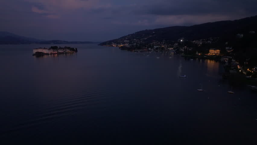 aerial dusk coastline with distant island and twinkling shoreline lights, calm reflective bay under purple clouds, sweeping