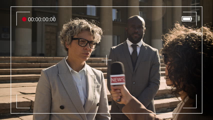 Medium shot with TV video camera frame effect of mature Caucasian female barrister refusing to comment on court trial to journalist with microphone, then black male bodyguard leading her away