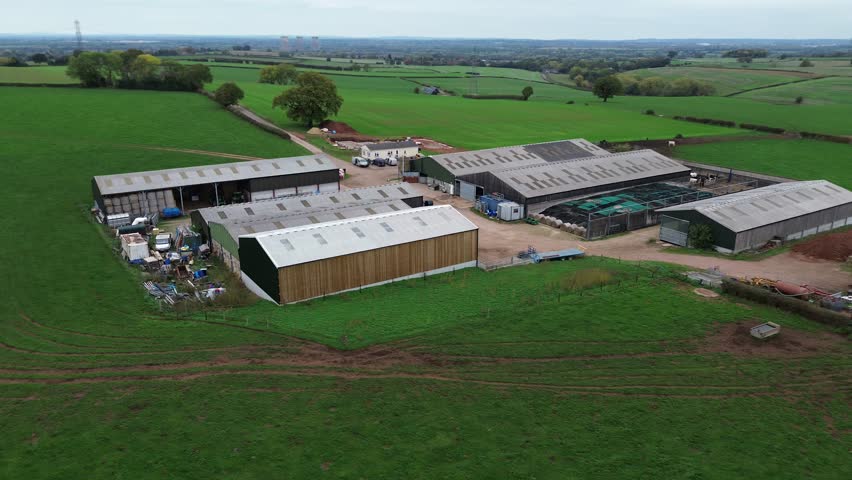 A farm with a lot of buildings and a large green field. The buildings are mostly white and the field is lush and green