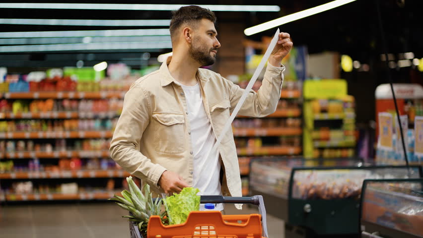 Man checking long shopping list receipt in supermarket