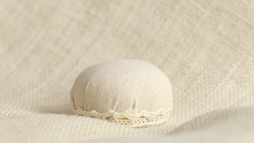 Woman stabbing pins into pincushion on light cloth, closeup