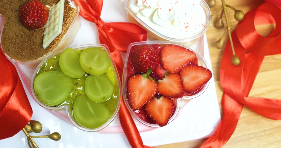 Heart shaped dessertstiramisu, fruity pastry, whipped creamnestled on wooden surface, accented by crimson ribbons, embodying romantic valentines mood