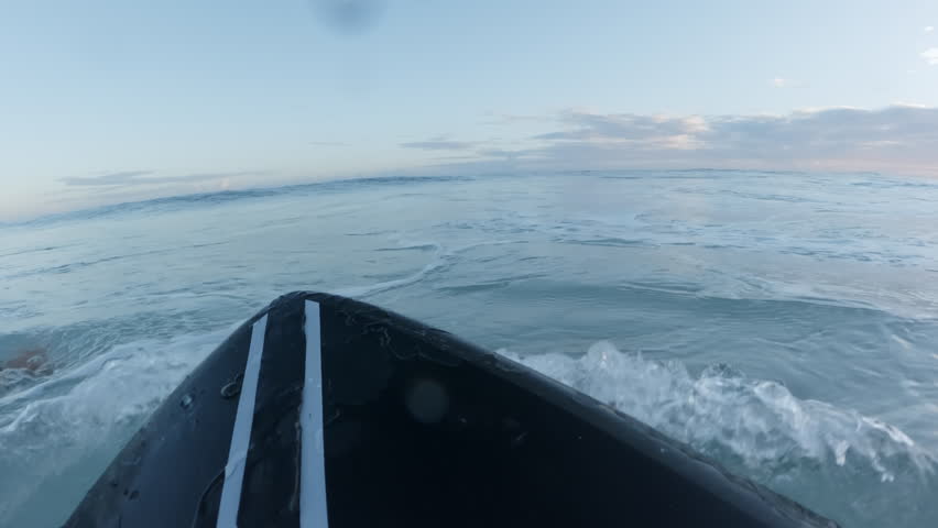 POV. Surfer on black surfboard swimming in line up looking at big wave in Atlantic ocean during sunrise.