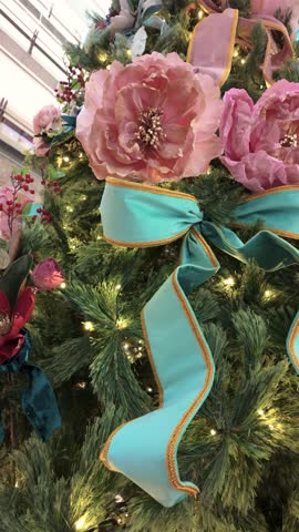 A festive Christmas tree adorned with lush greenery, soft pink roses, and a bold turquoise ribbon bow. 
