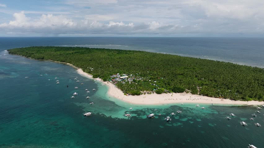 Tropical coastline with sandy beach lined with boats and palm trees near turquoise water. Daku Island. Siargao, Philippines.