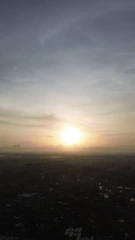 Sunrise aerial over small town with morning fog and soft golden light. Peaceful early day atmosphere with distant hills and rural settlement.