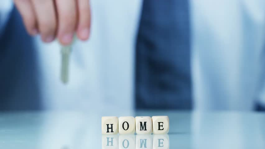 Slow-motion macro of wooden letter blocks spelling “My Home” with a new homeowner holding keys, symbolizing new home ownership and future.