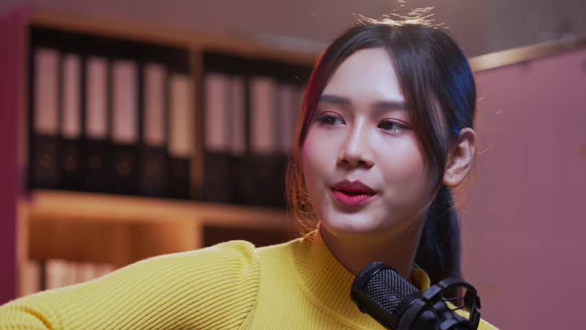 Young energetic asian woman singing and playing guitar in a music studio. Professional singer recording a new song in a soundproof room