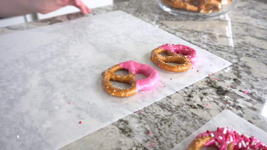 With focused attention, this budding culinary artist dips pretzels into a pot of melted chocolate, creating sweet delights in the warmth of a well-lit home kitchen.