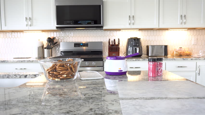 With focused attention, this budding culinary artist dips pretzels into a pot of melted chocolate, creating sweet delights in the warmth of a well-lit home kitchen.