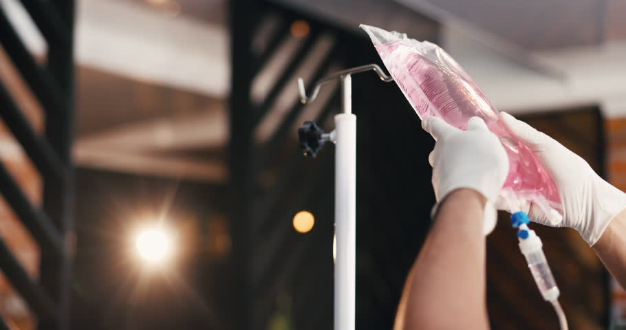 Wellness, doctor and hands in clinic with iv drip for medicine, patient treatment and hydration benefits. Flare, healthcare person and prepare intravenous bag with liquid, supplements and nutrients.