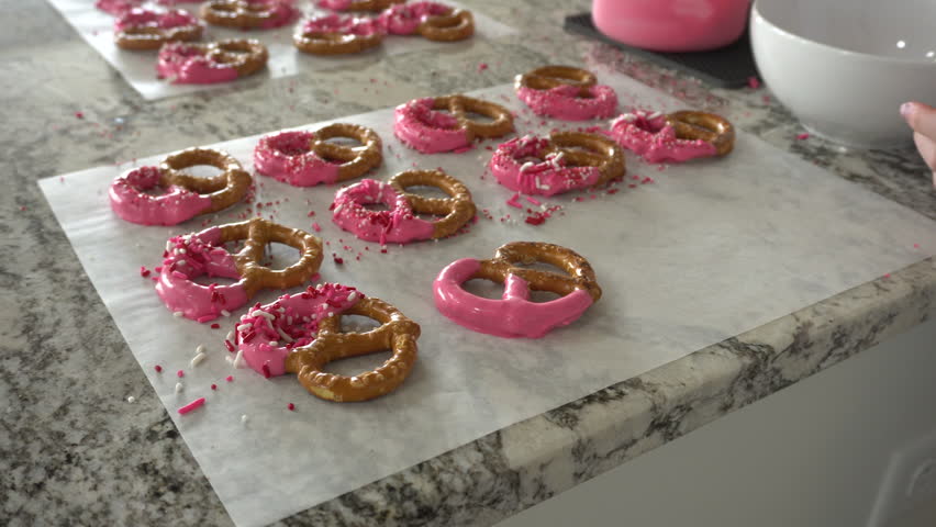 With focused attention, this budding culinary artist dips pretzels into a pot of melted chocolate, creating sweet delights in the warmth of a well-lit home kitchen.