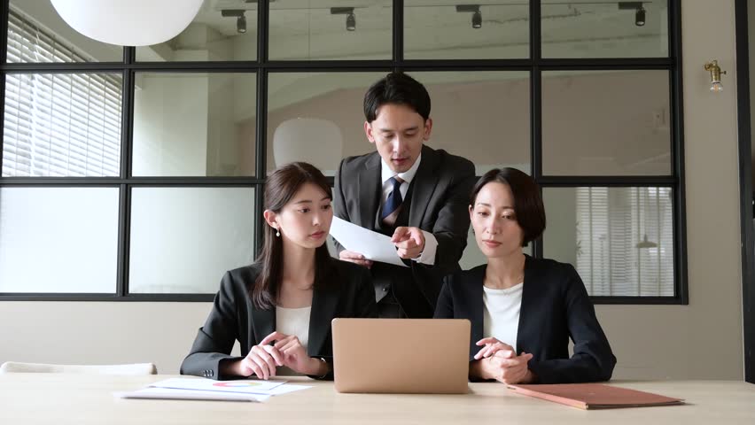 Japanese men and women having a meeting while looking at the computer in the office