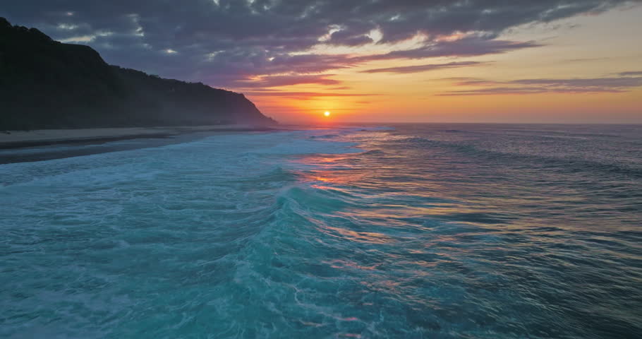 Indonesia, Bali: amazing beautiful sunset over ocean, painting sky with warm colors and reflecting on the turquoise waves breaking along the tropical coastline. Natural background. Aerial drone flight