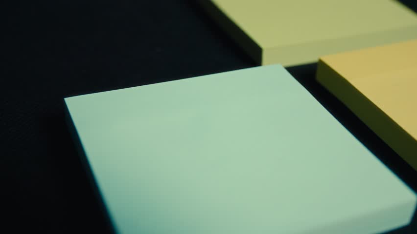 Smooth push-in close-up on a blue sticky note pad on a dark desk, selective focus for idea reminder and planning concept