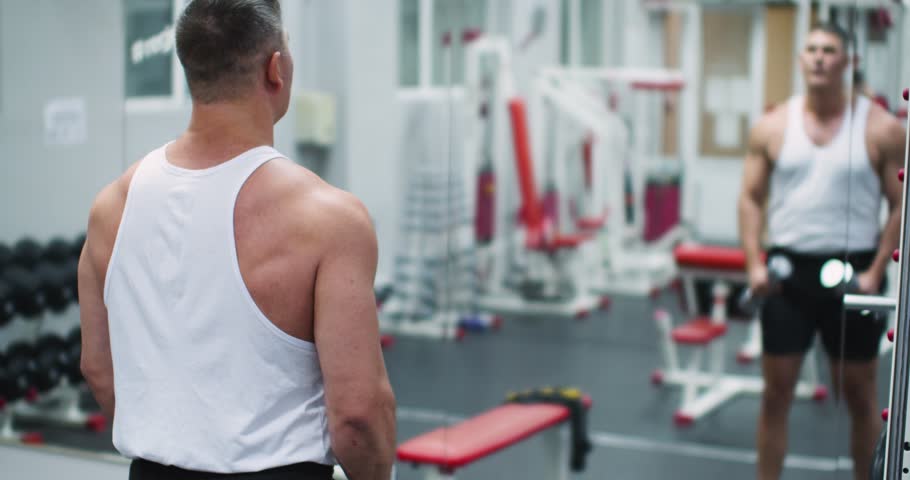 Dumbbell raises for the deltoid muscles. Deltoid workout with dumbbells. Slow motion 4k footage of a Caucasian man during gym workout in front of the mirror.