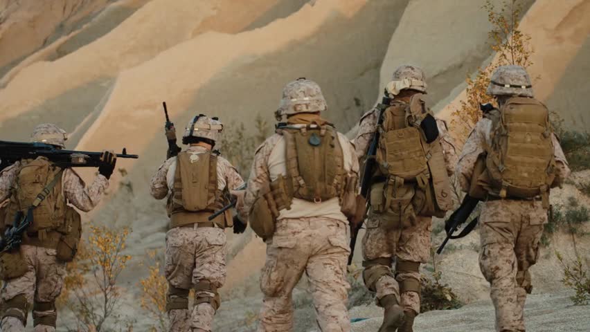 Group of fully equipped and armed soldiers walking toward the camera in a desert environment, showcasing military readiness, teamwork, and tactical operations.