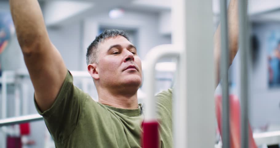 Slow motion cropped 4k footage of a middle aged Caucasian man working out in the gym. Workout for back muscles. Physical education as a norm of life for maintaining health.