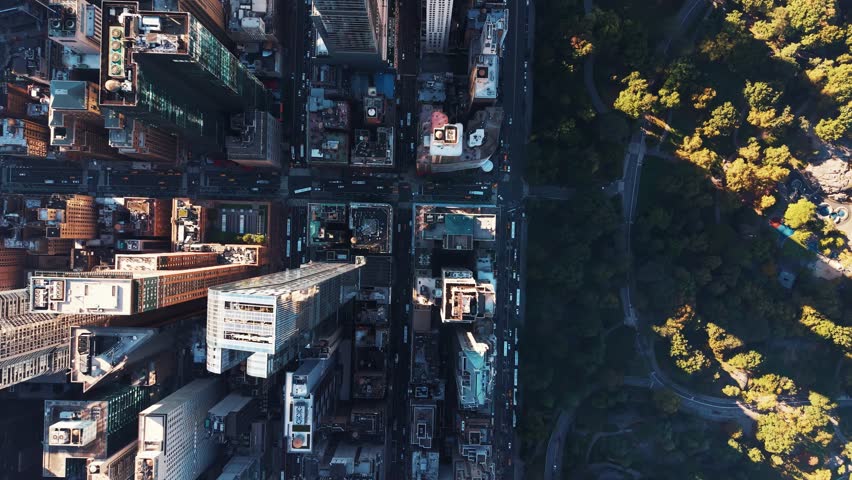 An extreme top down aerial view capturing the towering skyscrapers of Midtown Manhattan in New York City with the green space of Central Park visible in the corner