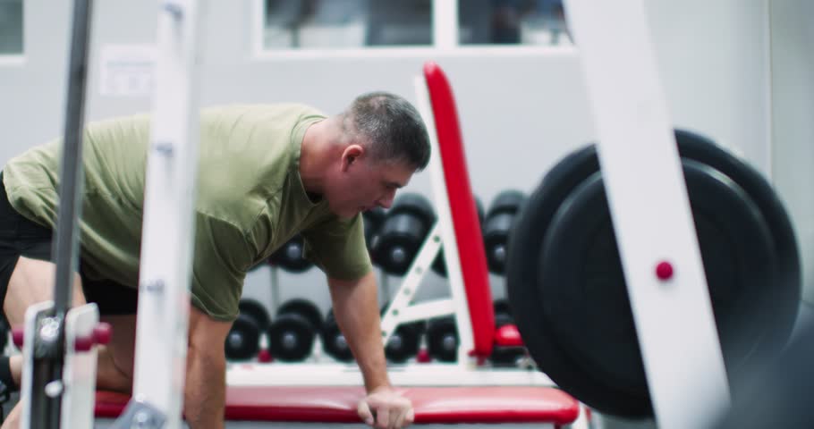 Slow motion video of a middle aged Caucasian man working out in the gym. Workout with a big dumbbell for back muscles. Physical education as a norm of life for maintaining health. Cropped 4k footage.