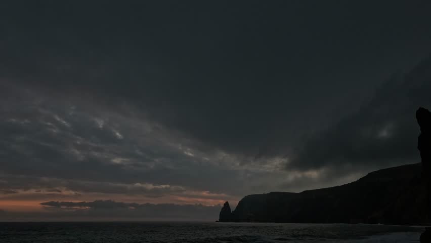 Dark ocean sunset with dramatic clouds moving over vast sea and silhouetted cliffs