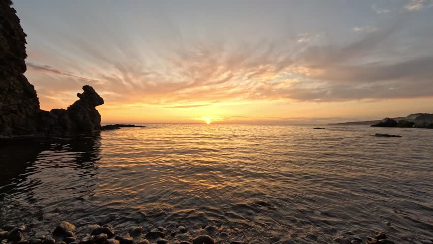 Sunset, Ocean, Beach golden hour light reflecting on calm sea waves over a rocky shore with picturesque clouds at dusk