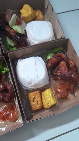 Top view of Indonesian lunch box catering containing white rice, fried tofu, vegetables, and savory side dishes in cardboard takeaway boxes. Suitable for food delivery, catering business, local cuisine, meal preparation, and culinary content.