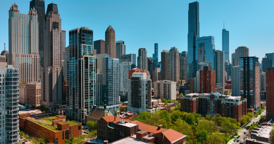 Fantastic view of diverse modern beautiful skyscrapers in the downtown of Chicago, Illinois, USA. Drone footage over the low-rise buildings among the lush greenery.