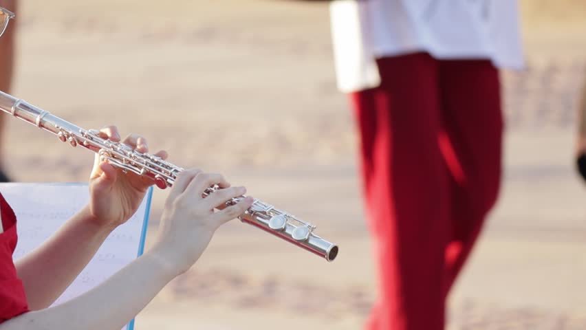 Close-up of hands playing a silver flute outdoors with people blurred in the background.