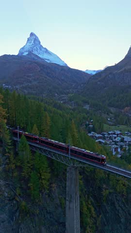 Rack Railway Red Train on Findelbachbrucke Bridge, Matterhorn Mountain and Larches in Autumn Evening. Swiss Alps. Aerial Drone Shot. Zermatt, Valais, Switzerland. Vertical Video