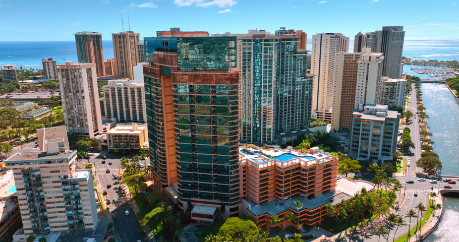 Multi-storied building with glass facades on the bank of Ala Wai Canal in Honolulu, Hawaii, USA. Sunny panorama of Waikiki from drone footage.