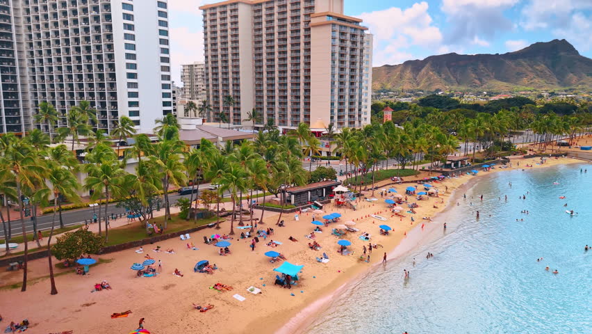 Idyllic sandy beach with palm trees and numerous vacationers. View on Waikiki, Honolulu, Hawaii, USA. Diamond Head Crater at backdrop. Aerial perspective.