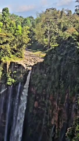 Majestic tropical waterfall cascade and lush green cliff face with a stunning rainbow appearing in the mist. Epic nature and travel footage.