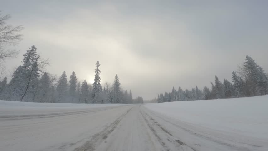View from the front of a vehicle while driving along a snow-covered road through a snowy northern forest