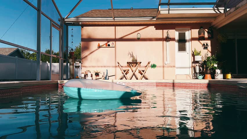 a peaceful backyard swimming pool sits beneath a screened patio, with an inflatable float drifting on clear water and warm sunlight reflecting across the space.