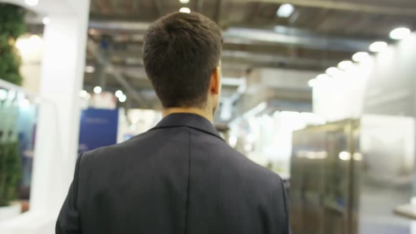 Young entrepreneur walks through a business fair, looking amazed at technology, finance, and trade exhibits, capturing curiosity, innovation, and professional exploration.