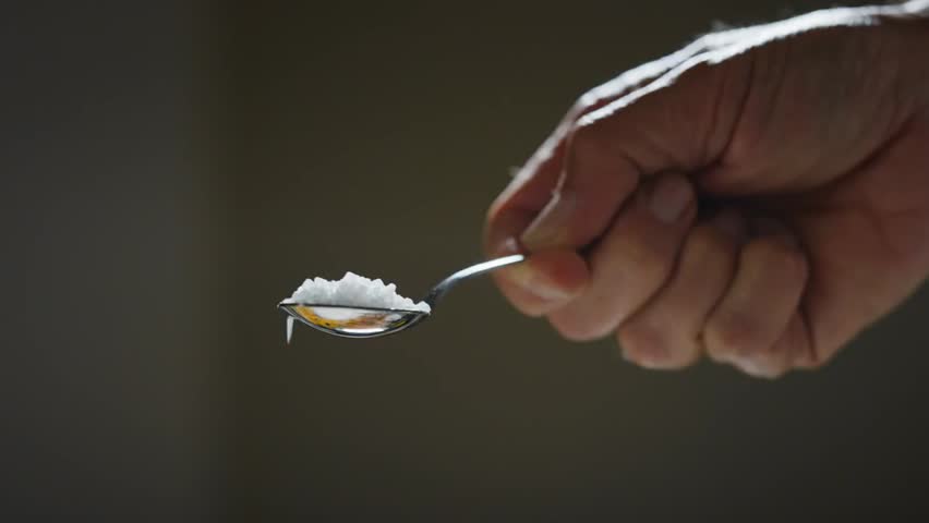 Close-up of a chef’s hand sprinkling salt with a teaspoon, highlighting precision, culinary technique, and the art of cooking with spices in a kitchen.