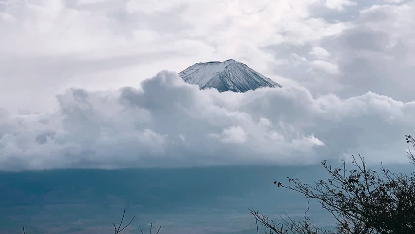 mount fuji emerges above a layer of soft clouds, creating a quiet and atmospheric scene beneath a pale sky in japan.